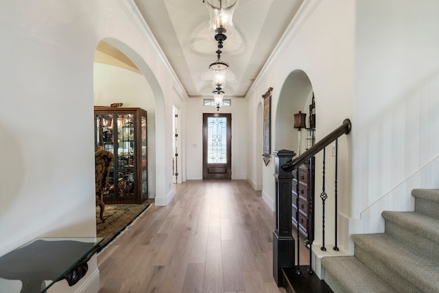 foyer entrance with arched walkways, crown molding, stairway, light wood-type flooring, and baseboards