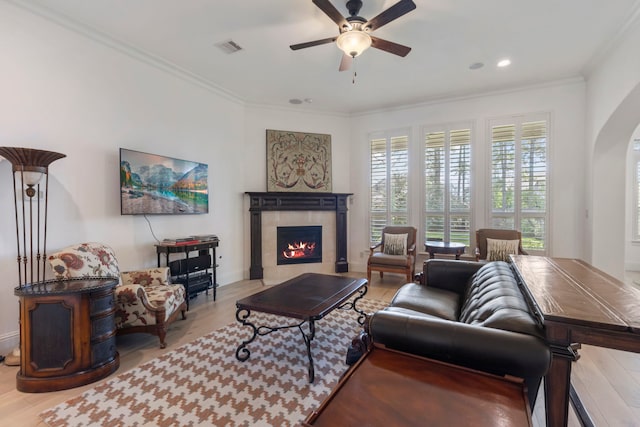 living area featuring visible vents, arched walkways, a tile fireplace, wood finished floors, and crown molding