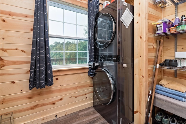 washroom with stacked washer / drying machine, laundry area, wooden walls, and wood finished floors