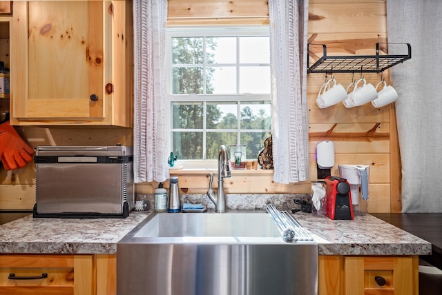 kitchen with light brown cabinets, light countertops, a sink, and wooden walls