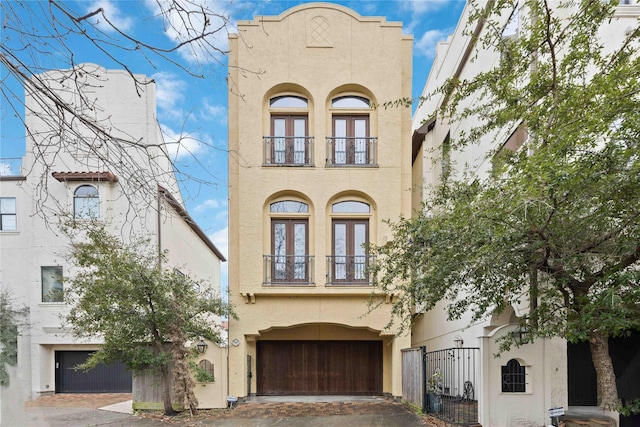 view of front of house with french doors, decorative driveway, stucco siding, a balcony, and a garage