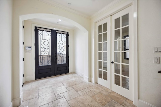 foyer entrance featuring stone tile floors, arched walkways, baseboards, ornamental molding, and french doors