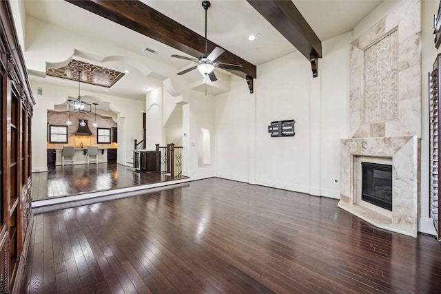 unfurnished living room featuring a premium fireplace, wood-type flooring, beam ceiling, and a ceiling fan