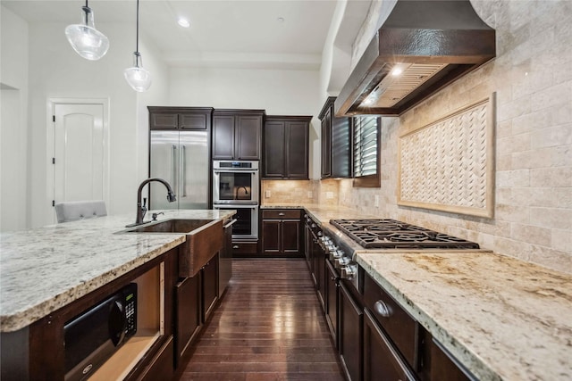 kitchen featuring dark wood-style floors, decorative backsplash, appliances with stainless steel finishes, light stone countertops, and wall chimney exhaust hood