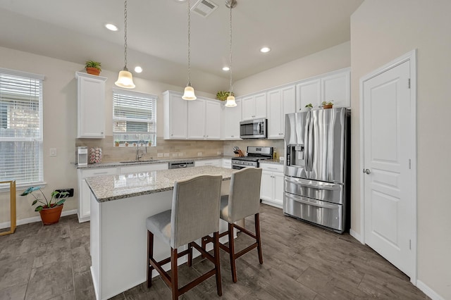 kitchen with tasteful backsplash, visible vents, appliances with stainless steel finishes, a sink, and a kitchen island