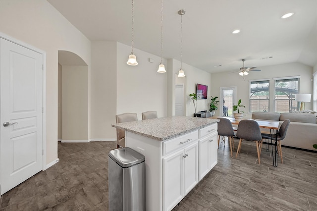 kitchen featuring arched walkways, open floor plan, decorative light fixtures, a center island, and white cabinetry