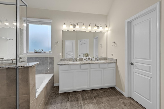 full bath with double vanity, a garden tub, a sink, and wood finished floors