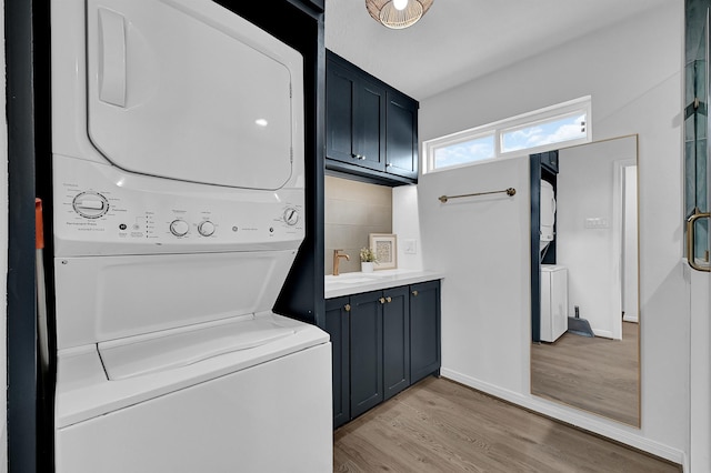 laundry area featuring laundry area, baseboards, stacked washer and clothes dryer, light wood-style floors, and a sink