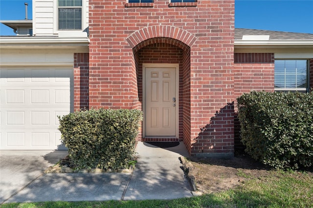 doorway to property with a garage, brick siding, and a shingled roof