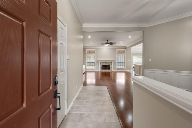 entrance foyer with a ceiling fan, wainscoting, crown molding, light wood-style floors, and a fireplace