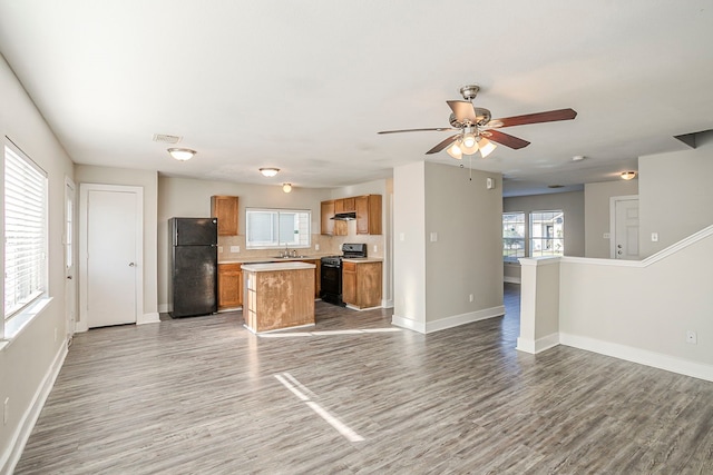 kitchen with wood finished floors, open floor plan, decorative backsplash, a center island, and black appliances