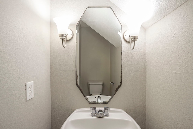 half bath with a textured wall and a sink