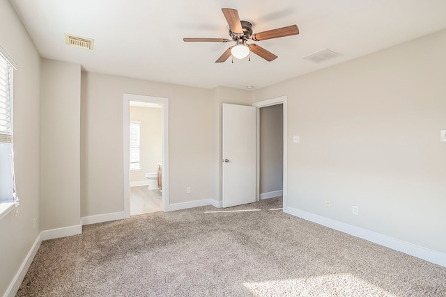 unfurnished bedroom featuring baseboards, ensuite bath, visible vents, and light colored carpet