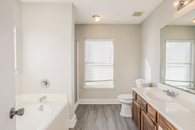 bathroom featuring toilet, wood finished floors, visible vents, vanity, and a bath