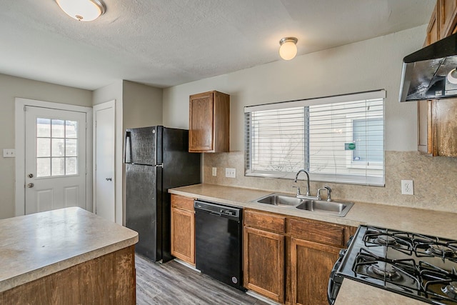 kitchen with light countertops, backsplash, light wood-style floors, a sink, and black appliances