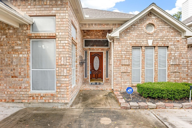 property entrance featuring a shingled roof and brick siding