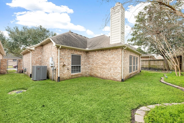 back of property featuring a lawn, a chimney, fence private yard, central AC, and brick siding