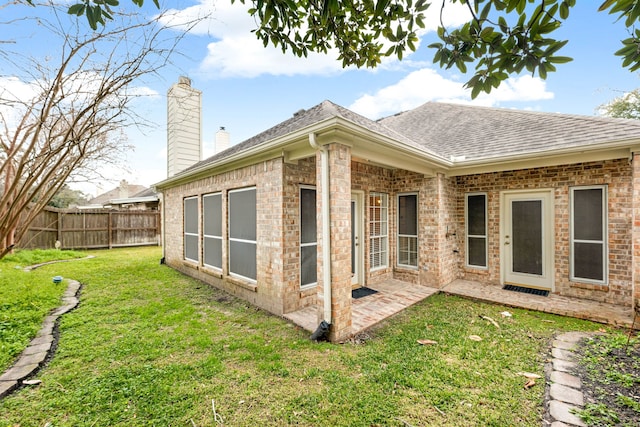 back of house featuring brick siding, a patio, a chimney, a lawn, and fence