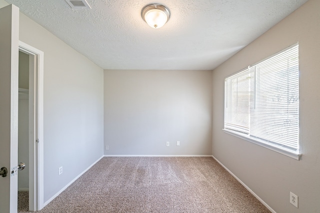 carpeted spare room featuring visible vents, a textured ceiling, and baseboards