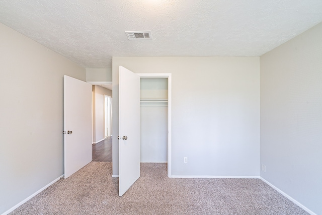 unfurnished bedroom featuring baseboards, visible vents, a textured ceiling, carpet floors, and a closet