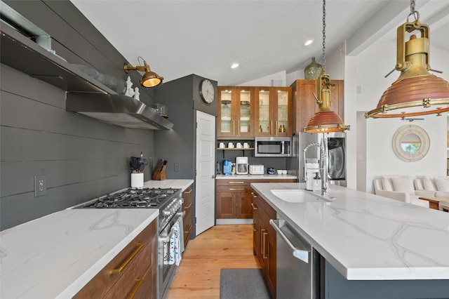 kitchen with brown cabinetry, appliances with stainless steel finishes, vaulted ceiling, light wood-style floors, and a sink