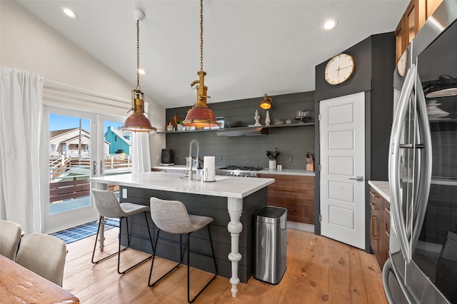 kitchen featuring light wood-style floors, light countertops, brown cabinets, stainless steel fridge, and a kitchen bar