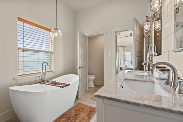 bathroom with double vanity, toilet, a freestanding bath, a healthy amount of sunlight, and a sink