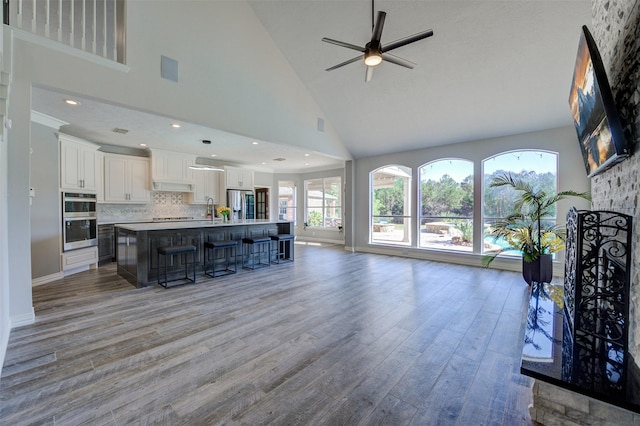 living area with baseboards, ceiling fan, wood finished floors, a fireplace, and high vaulted ceiling