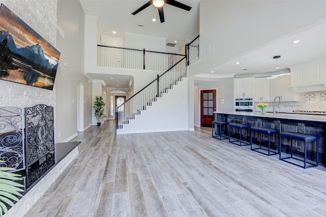 living area with ceiling fan, baseboards, stairs, light wood-style floors, and ornamental molding