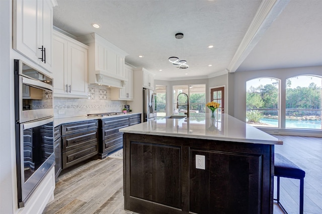 kitchen with crown molding, light wood finished floors, stainless steel appliances, decorative backsplash, and a sink