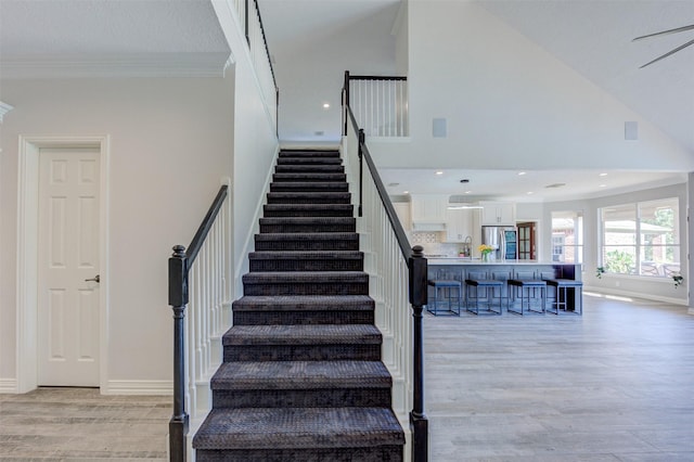 stairway with baseboards, wood finished floors, crown molding, high vaulted ceiling, and recessed lighting