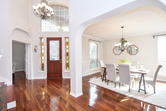 foyer entrance featuring a high ceiling, arched walkways, ornamental molding, wood-type flooring, and a chandelier