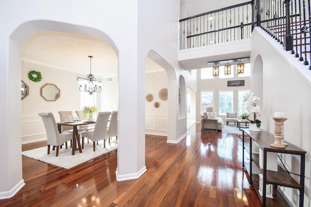 foyer featuring hardwood / wood-style floors, arched walkways, a towering ceiling, a decorative wall, and a chandelier