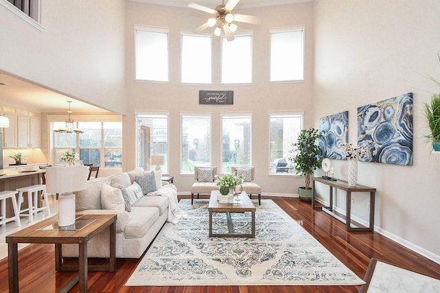 living room featuring a high ceiling, dark wood-style floors, ceiling fan with notable chandelier, and baseboards