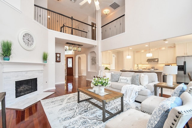 living room featuring visible vents, baseboards, ceiling fan, arched walkways, and dark wood-style floors