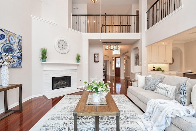 living area with arched walkways, baseboards, a chandelier, dark wood-style flooring, and a tile fireplace