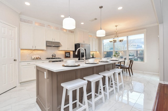 kitchen with visible vents, stainless steel appliances, decorative backsplash, under cabinet range hood, and a kitchen breakfast bar