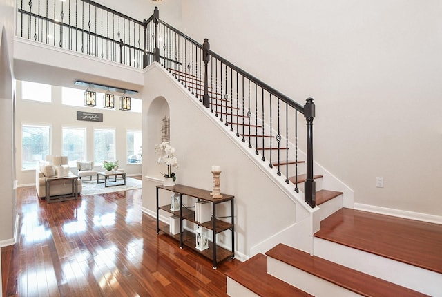 stairs with arched walkways, a high ceiling, baseboards, and hardwood / wood-style flooring