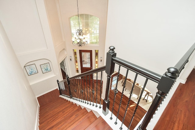 staircase featuring baseboards, a notable chandelier, wood finished floors, and a towering ceiling