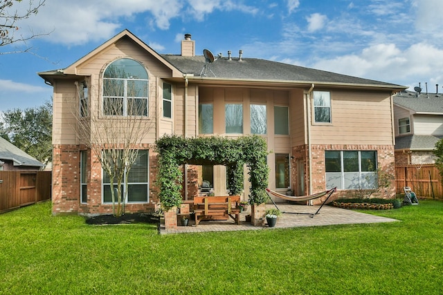 rear view of house featuring brick siding, a patio area, a lawn, and fence