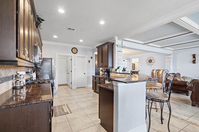 kitchen with a breakfast bar area, gas range oven, visible vents, stainless steel microwave, and a peninsula