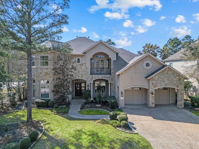 french country home featuring concrete driveway, a front yard, french doors, a balcony, and an attached garage