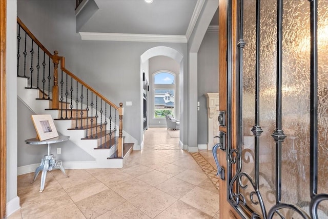 entrance foyer featuring baseboards, arched walkways, crown molding, and stairway