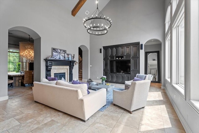 living area with baseboards, arched walkways, a glass covered fireplace, beamed ceiling, and a chandelier