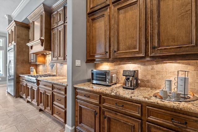 kitchen featuring backsplash, crown molding, a toaster, light stone counters, and stainless steel appliances