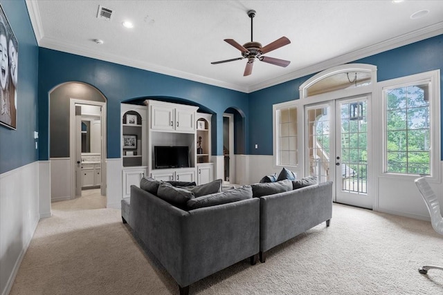 living room featuring arched walkways, ornamental molding, french doors, wainscoting, and light colored carpet