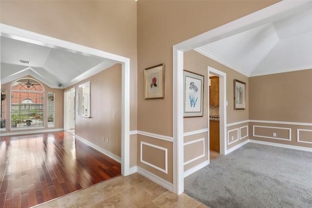 hallway featuring lofted ceiling, carpet floors, crown molding, and a decorative wall