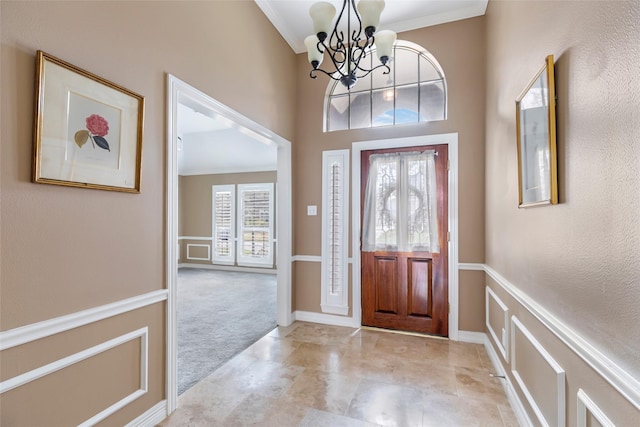 entryway featuring light carpet, a chandelier, baseboards, and ornamental molding