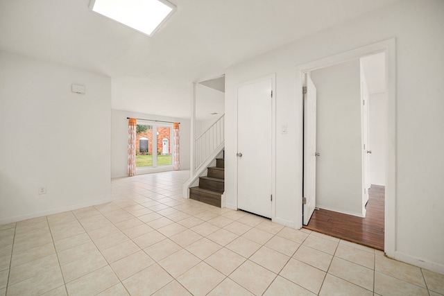 unfurnished room with stairway, light tile patterned flooring, and baseboards