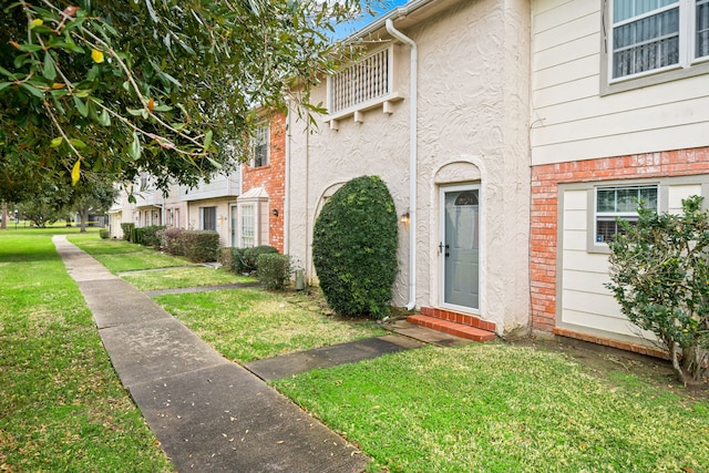 view of exterior entry with a yard and stucco siding